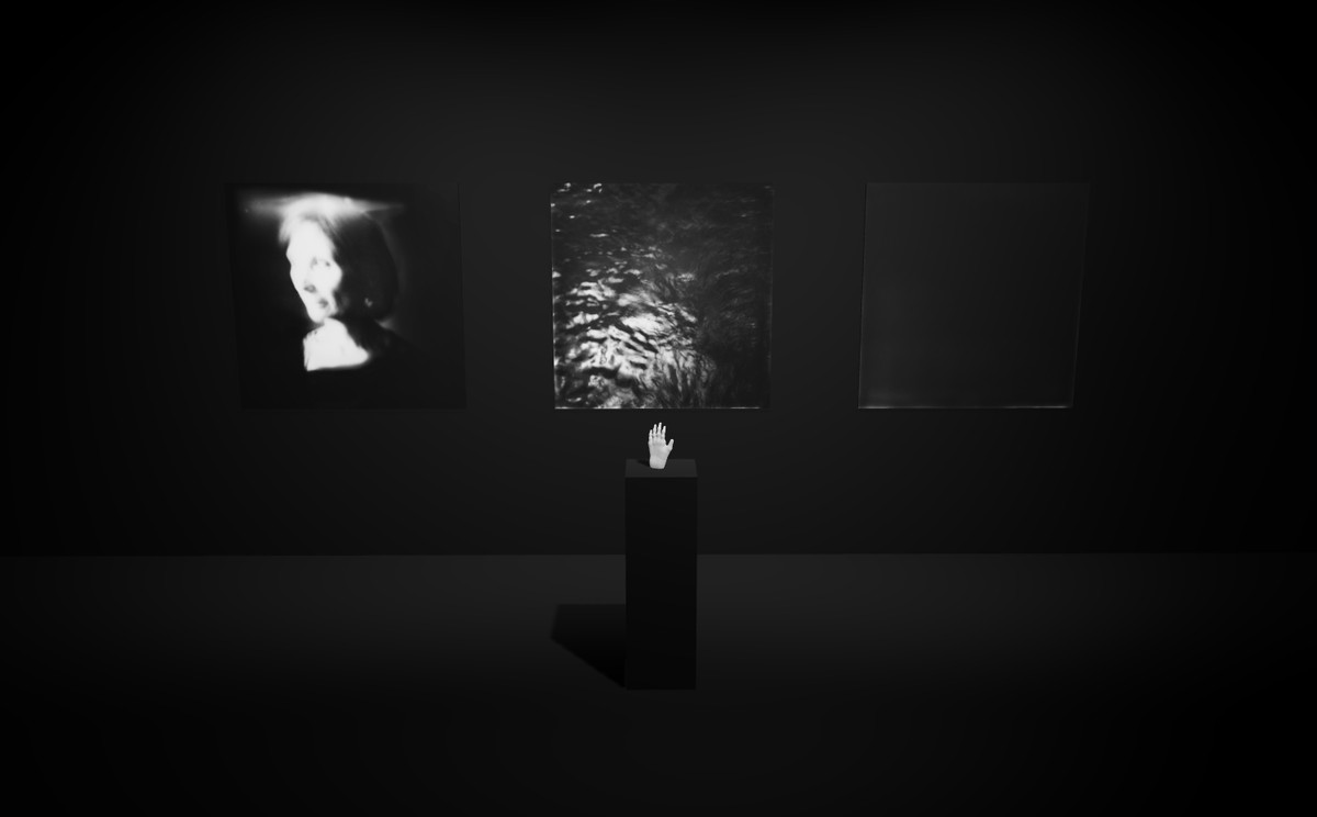 Digital reconstruction of the 2016 exhibition: in a black room, three black-and-white photographs hang on the wall, a face, agitated water, an almost entirely dark image, and in front of them a plinth carrying a hand cast in resin, standing upright.