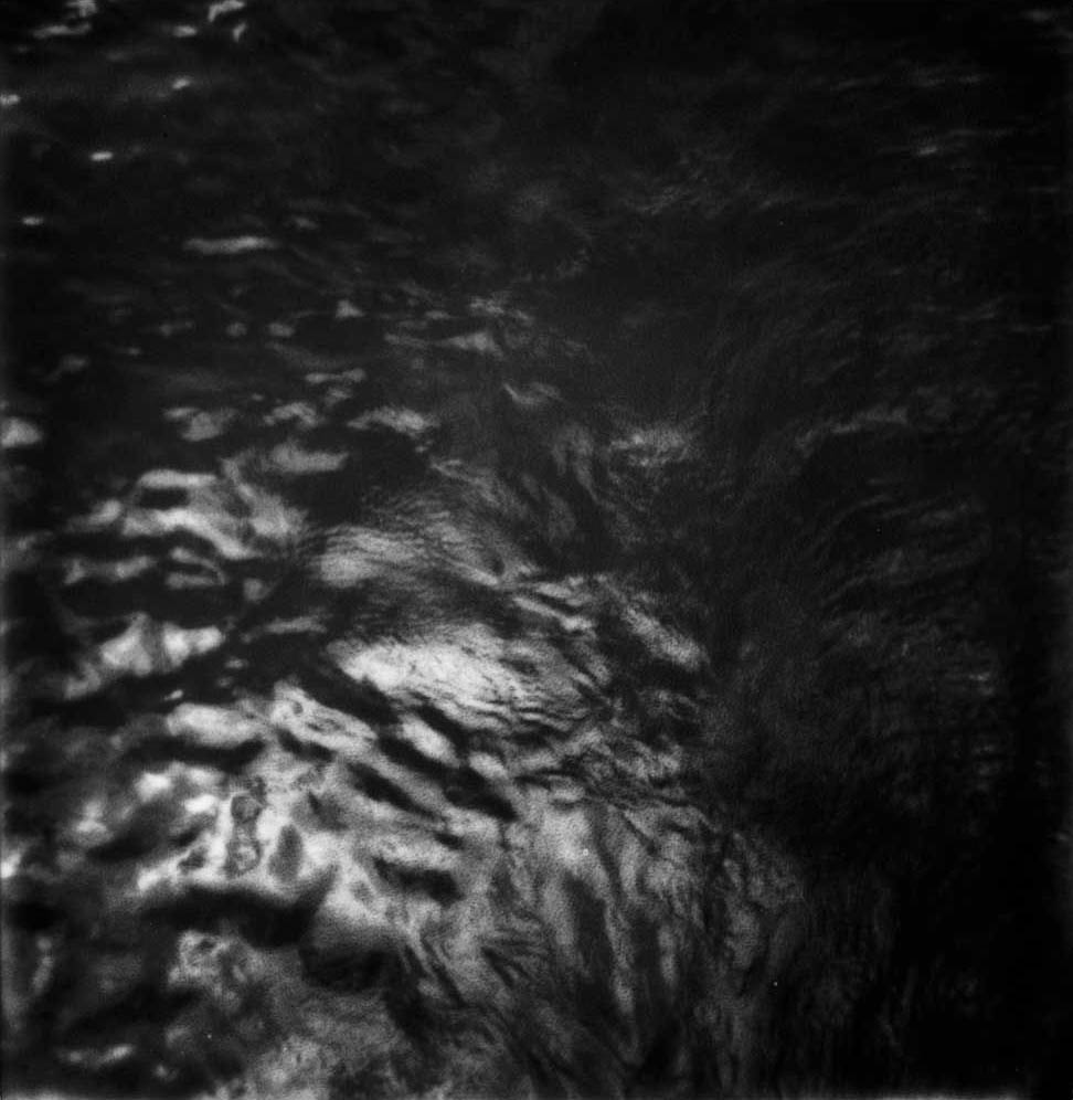 Agitated water surface in black and white: pale reflections dissolve into a dark mass, with no identifiable object.