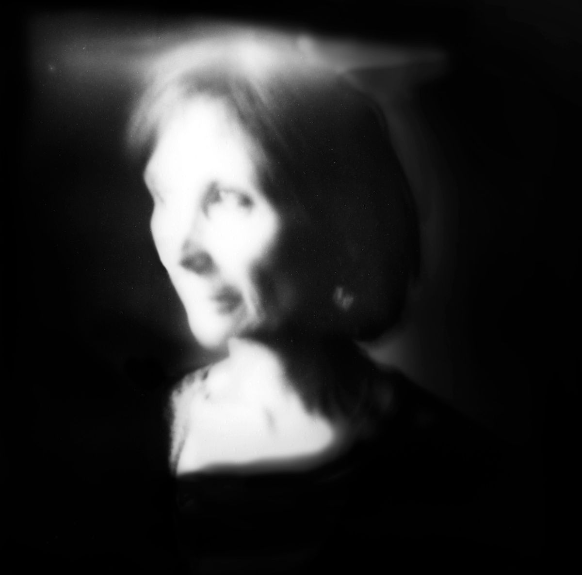 Blurred black-and-white portrait: a face in profile barely stands out from the dark, held at the threshold of legibility.
