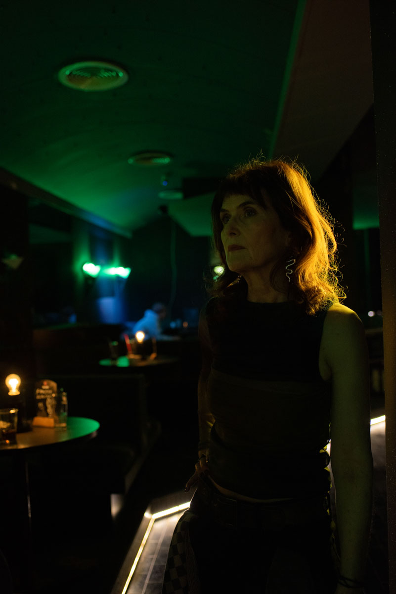 A woman in profile in a bar lit in green, her hair backlit.