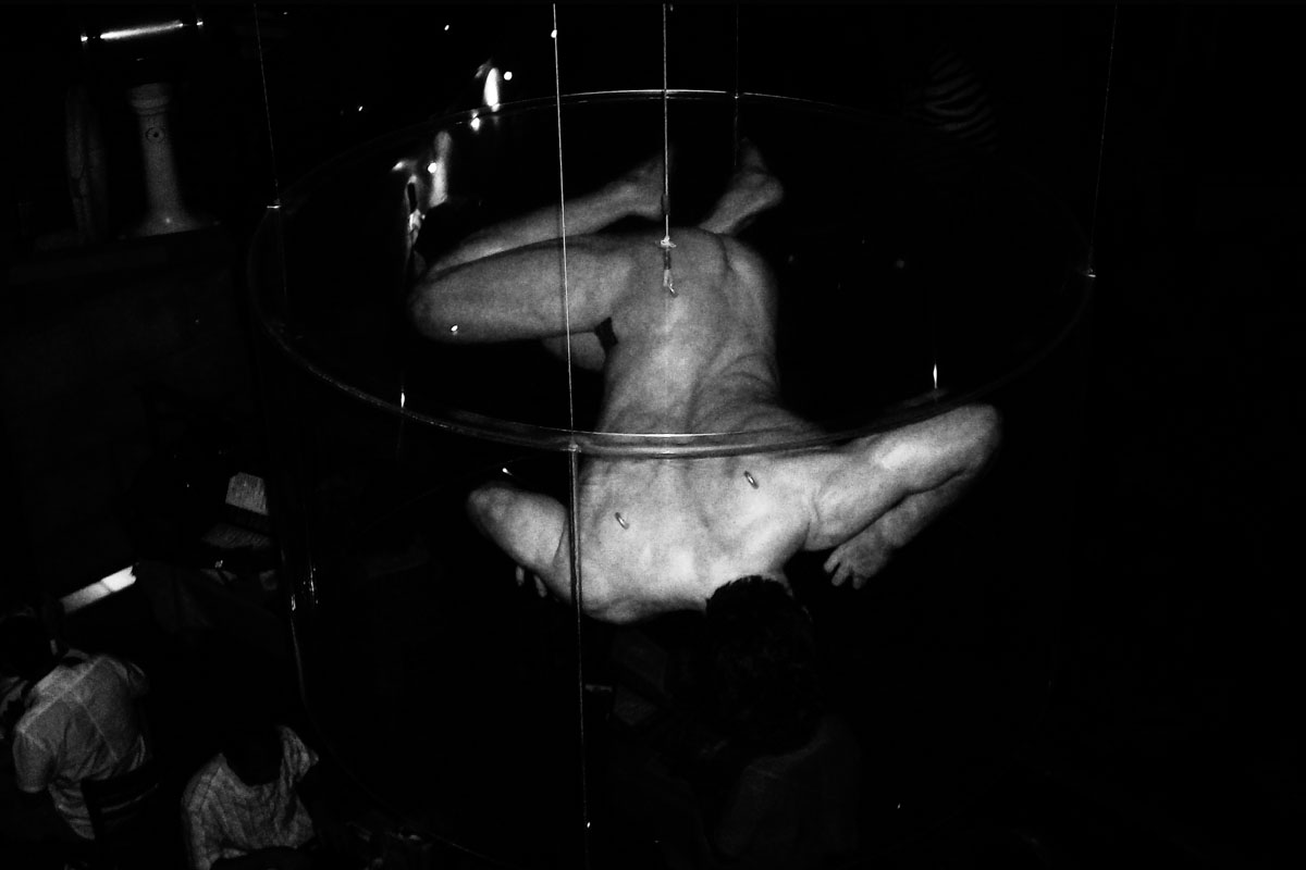 A naked body suspended in a metal hoop above spectators.