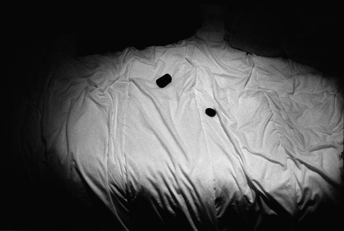 A crumpled white sheet on a bed, two small dark objects lying on it.