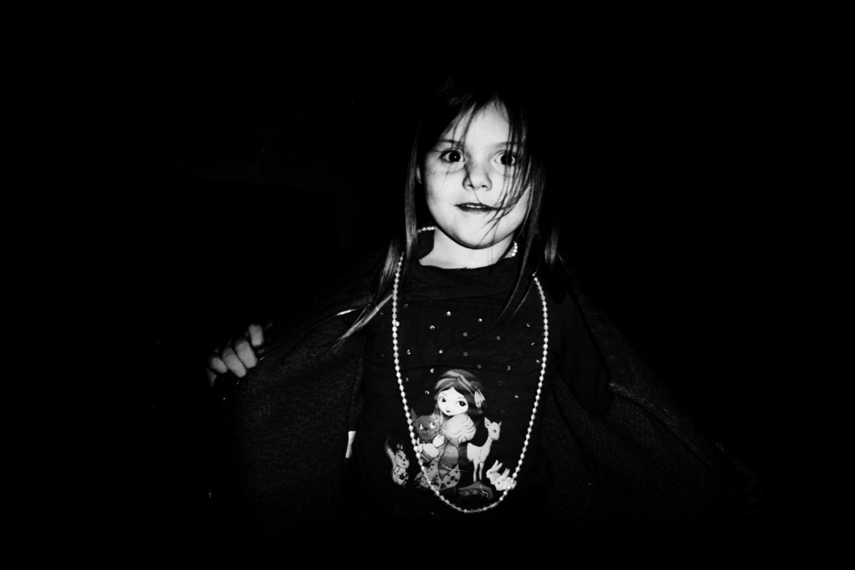 A little girl in the dark, a string of beads over her jumper.