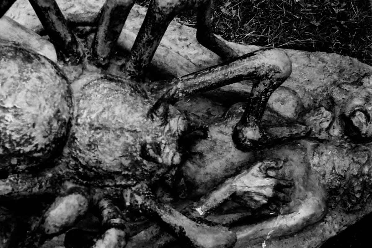 Close view of a sculpture: bodies entangled beneath the legs of a creature.
